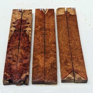 Könnte beinhalten: Drei Sätze Holzrohlinge für Holzbearbeitungsprojekte. Jedes Set besteht aus zwei Holzstücken mit einzigartigen Maserungen. Das Holz ist rotbraun mit dunkleren braunen und schwarzen Streifen.