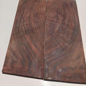 May include: Two rectangular pieces of wood with a rich, dark brown color and intricate grain patterns. The wood has a reddish hue in some areas, creating a visually appealing contrast. The pieces are placed side by side.