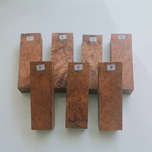 Pode incluir: Sete blocos de madeira, cada um com um número de 1 a 7 escrito nele. Os blocos estão dispostos em uma fila, com os números aumentando da esquerda para a direita. Os blocos são todos feitos do mesmo tipo de madeira, que tem uma cor marrom avermelhada e um padrão de grão natural.