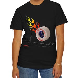 Può includere: T-shirt nero con grafica di una ruota di pattino a rotelle in fiamme e la scritta "All American Dream". Il design include una silhouette dello skyline e stelle rosse.