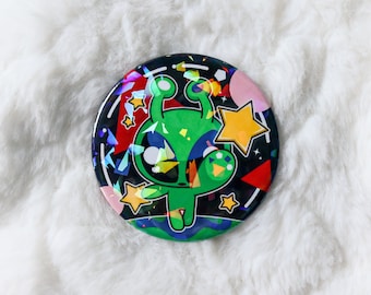 May include: A round button with a green alien character with large eyes and antennas. The alien is surrounded by colorful geometric shapes and stars on a black background.