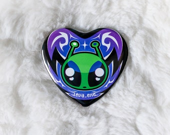 May include: A heart-shaped pin with a green alien with black eyes and a purple and blue background. The text "Leva.exe" is printed on the pin.