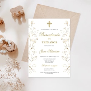Peut inclure: Une invitation blanche avec des accents floraux dorés et du texte en espagnol. La carte présente une croix et les mots "Presentación de Tres Años" (Présentation de trois ans). Des jouets en bois et une enveloppe beige sont en arrière-plan.
