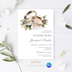 以下が含まれることがあります： 金色の指輪と白い花が描かれた結婚式の招待状。「Nuestra Boda」の文字と、Jazmin & Carlosの名前、日付、時間、場所が記載されています。招待状は花の要素とCanvaのロゴで装飾されています。
