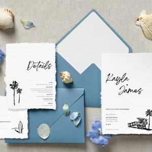 May include: A beach-themed wedding invitation suite with white cards, blue envelopes, and seashell accents. The invitation cards feature black text and illustrations of palm trees, a lifeguard stand, and a surfboard. The suite includes RSVP and details cards.