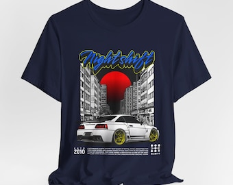 May include: A navy blue t-shirt with a white car and city skyline graphic. The graphic features a red sun and the text "Night Shift" in yellow and blue. The text "2010" is also included in the graphic.