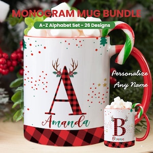 May include: White ceramic mug with a red handle and rim, featuring a large plaid letter "A" and the name "Amanda". The mug has a Christmas theme with deer antlers and festive accents. A smaller mug with the letter "B" and the name "Bruna" is also shown.