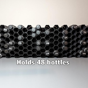 May include: A black honeycomb-shaped storage rack holds 48 bottles. The rack is made of plastic and has a modern design. The bottles are not included.