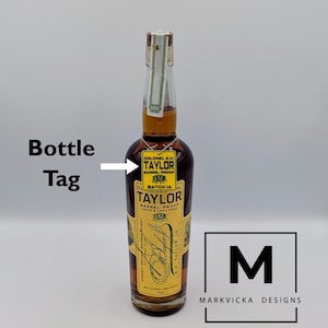 May include: A brown glass bottle of Colonel E.H. Taylor Barrel Proof bourbon whiskey. The bottle has a yellow label with black text and a silver chain tag. The bottle is sealed with a green and white striped top.