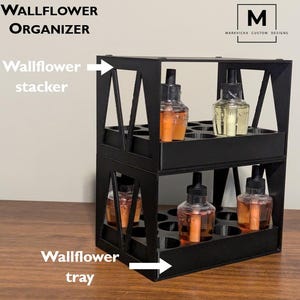 K&ouml;nnte beinhalten: Schwarzer Wand-Duft&ouml;l-Organizer aus Metall mit zwei Ebenen. Die obere Ebene ist mit "Wallflower stacker" und die untere Ebene mit "Wallflower tray" beschriftet.