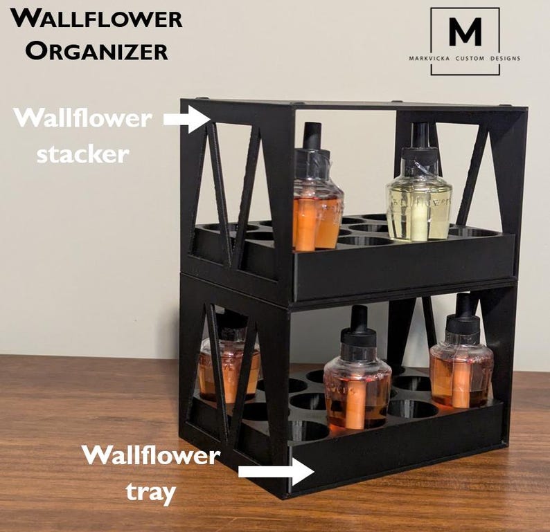 K&ouml;nnte beinhalten: Schwarzer Wand-Duft&ouml;l-Organizer aus Metall mit zwei Ebenen. Die obere Ebene ist mit "Wallflower stacker" und die untere Ebene mit "Wallflower tray" beschriftet.