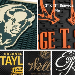 Pu&ograve; includere: Una collezione di tappetini da bar in gomma nera. Un tappetino presenta una testa di bisonte, un altro il testo "12"x12" SERVICE MAT", e altri mostrano nomi di marchi in vari colori. I tappetini misurano circa 30 cm x 30 cm.