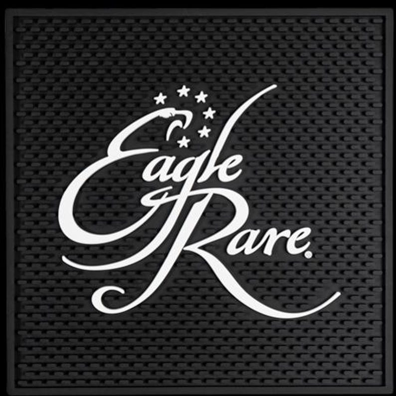 Pu&ograve; includere: Tappetino da bar nero con superficie strutturata. Il testo bianco "Eagle Rare" &egrave; visualizzato in una sceneggiatura stilizzata, con una testa d'aquila e stelle sopra la parola "Eagle".