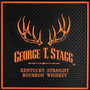 Pu&ograve; includere: Tappetino da bar nero con bordo arancione e motivo ripetuto. Il tappetino presenta il testo "GEORGE T. STAGG" e "KENTUCKY STRAIGHT BOURBON WHISKEY" in arancione, insieme a un design a corna.