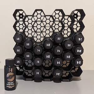 May include: Black hexagonal storage rack with 20 small bottles labeled with numbers. The bottles are arranged in a honeycomb pattern. A small bottle labeled "7-0" is in the foreground.
