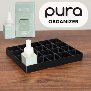 May include: A black organizer with multiple compartments, holding a fragrance refill bottle. The bottle and packaging are light green with the text "Linens & Surf". The word "pura" is visible on the packaging and the organizer.