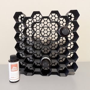 May include: Black honeycomb-shaped storage organizer with two small bottles inside. The bottles are labeled "the demi" and have a brown and white label.