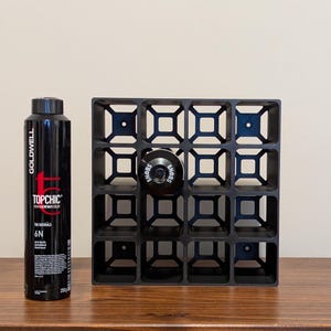 May include: A black metal wine rack with a grid pattern and 16 compartments. The rack is empty except for a black bottle stopper in the top center compartment. The rack is sitting on a wooden surface.