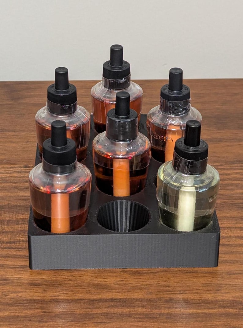 K&ouml;nnte beinhalten: Ein schwarzer Plastikhalter mit sechs durchsichtigen Glasflaschen mit schwarzen Kappen und Tropfern. Die Flaschen sind mit verschiedenen Fl&uuml;ssigkeiten gef&uuml;llt, darunter braun, orange und klar.