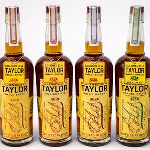 May include: Four bottles of Colonel E.H. Taylor bourbon. Each bottle has a brown glass body with a yellow label and a gold neck tag. The labels read "Small Batch", "Single Barrel", "Barrel Proof", and "Singight Rye".