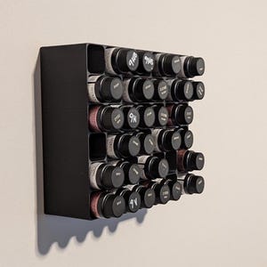 May include: A black wall-mounted organizer with 36 small glass bottles, each with a black lid and white lettering. The bottles are arranged in a grid pattern.