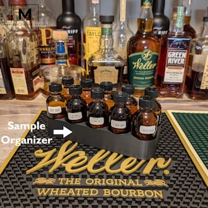 May include: A black sample organizer holding several small bottles of liquor. The organizer sits on a black bar mat with the word "Weller" in gold lettering. The mat also has the text "THE ORIGINAL WHEATED BOURBON".