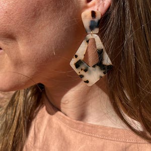 May include: A pair of geometric shaped earrings with a tortoiseshell pattern. The earrings are made of a light brown and white material.