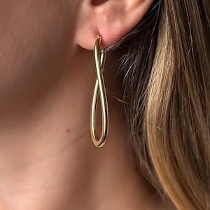 Op de afbeelding: Gouden oneindigheids-knoop oorbellen. De oorbellen zijn van een eenvoudig, elegant ontwerp.