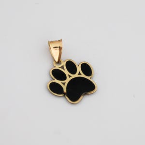 May include: Gold-coloured pendant in the shape of a paw print with black enamel filling. The pendant has a small loop at the top for a chain. The paw print design is a popular symbol for pet lovers.