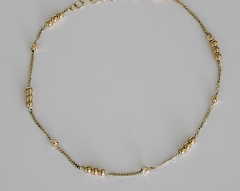 May include: Delicate gold-toned bracelet featuring a chain interspersed with small, round beads. The bracelet has a simple clasp and is displayed against a plain white background. A classic piece of jewelry.