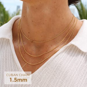 May include: Three layered gold-toned Cuban chains worn around the neck. The chains feature a delicate link design with a thickness of 1.5mm as indicated by the text overlay. The necklaces are worn over a white textured collared shirt.