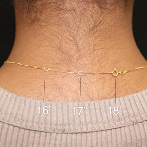 May include: A gold-colored chain necklace with a clasp, shown against a person's neck. The necklace is available in 16", 17", and 18" lengths. The necklace is a delicate, thin chain.