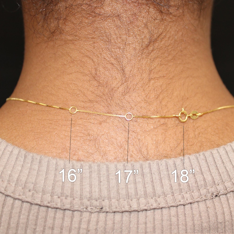 May include: A gold-colored chain necklace with a clasp, shown against a person's neck. The necklace is available in 16", 17", and 18" lengths. The necklace is a delicate, thin chain.