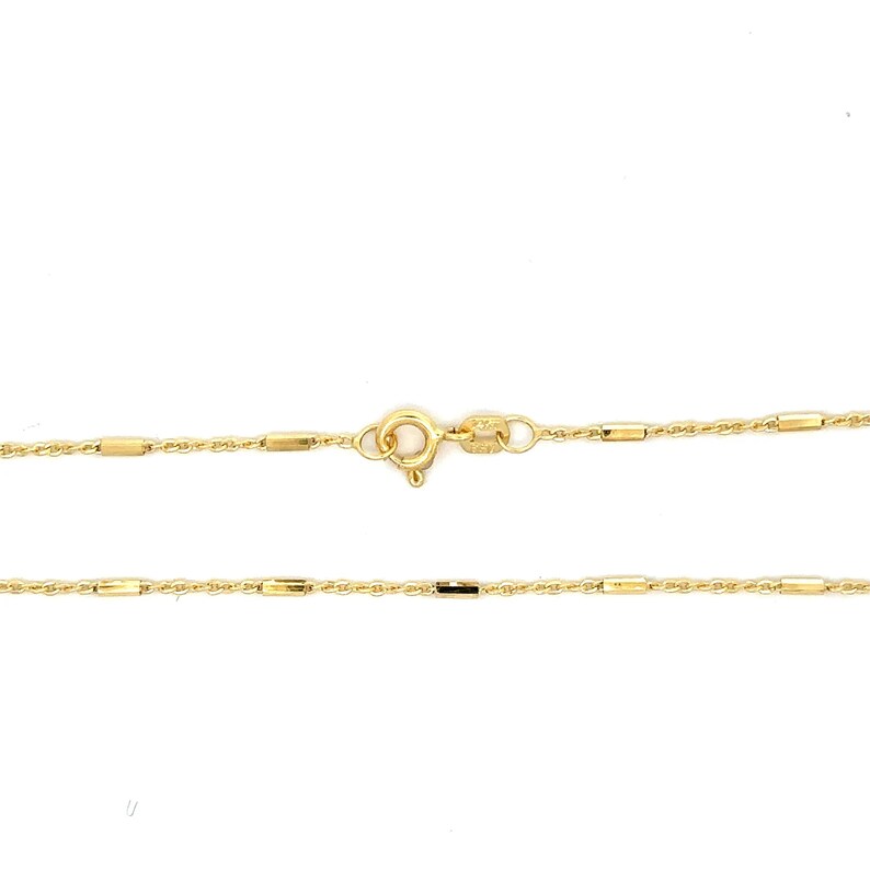 Puede incluir: Un collar de cadena de oro que presenta una serie de peque&ntilde;as cuentas cil&iacute;ndricas pulidas espaciadas uniformemente a lo largo de una delicada cadena de eslabones trenzados. Incluye un cierre de resorte circular y una peque&ntilde;a etiqueta rectangular.