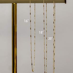 Puede incluir: Tres cadenas de tono dorado con peque&ntilde;os eslabones cil&iacute;ndricos espaciados uniformemente. Las cadenas se muestran en longitudes de 16, 18 y 20 pulgadas, con las medidas correspondientes claramente impresas junto a cada cadena individual.