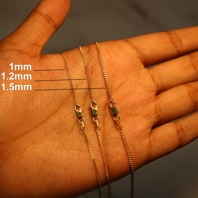 May include: Three gold-colored metal chains with lobster claw clasps, displayed with text labels indicating widths of 1mm, 1.2mm, and 1.5mm. The chains feature a delicate link design and are arranged side-by-side to show the size variation.