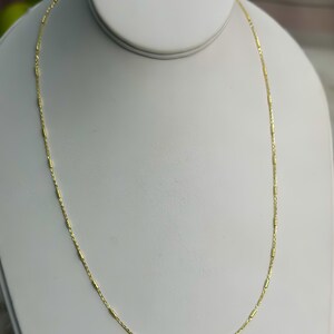 Puede incluir: Un delicado collar de cadena de oro que presenta una serie de peque&ntilde;os eslabones cil&iacute;ndricos espaciados uniformemente, conectados por finos eslabones circulares de alambre. La cadena tiene un acabado met&aacute;lico brillante y se muestra en un bucle.