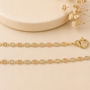 Puede incluir: Un delicado collar de cadena dorada con eslabones ovalados alternos con detalles tricolores de oro, oro rosa y plata. El collar tiene un cierre de mosquet&oacute;n y se muestra sobre un fondo neutro.