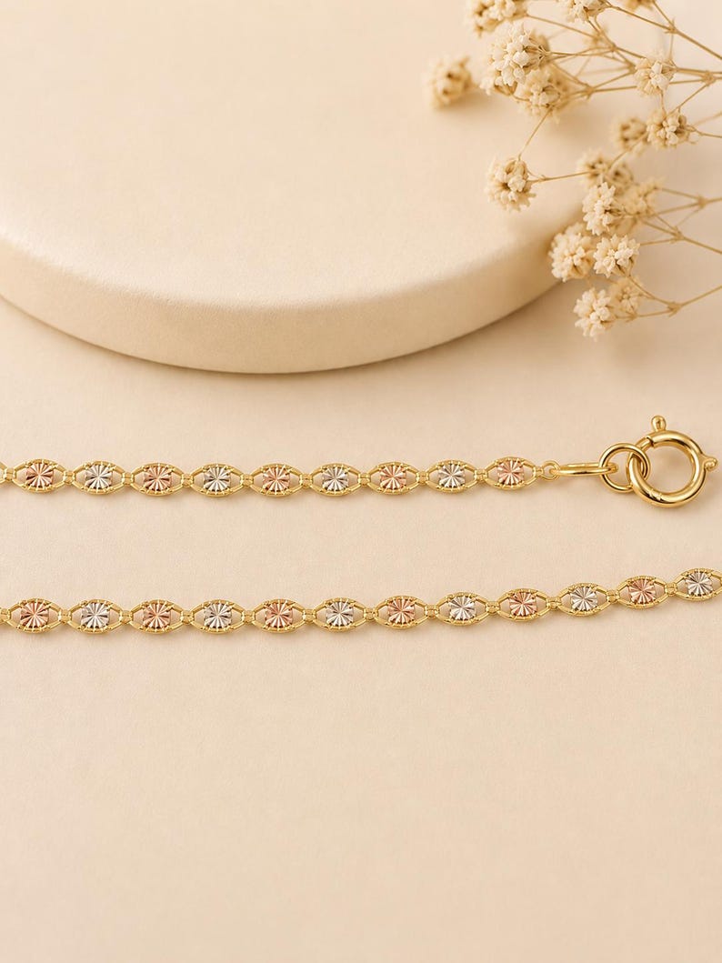 Puede incluir: Un delicado collar de cadena dorada con eslabones ovalados alternos con detalles tricolores de oro, oro rosa y plata. El collar tiene un cierre de mosquet&oacute;n y se muestra sobre un fondo neutro.