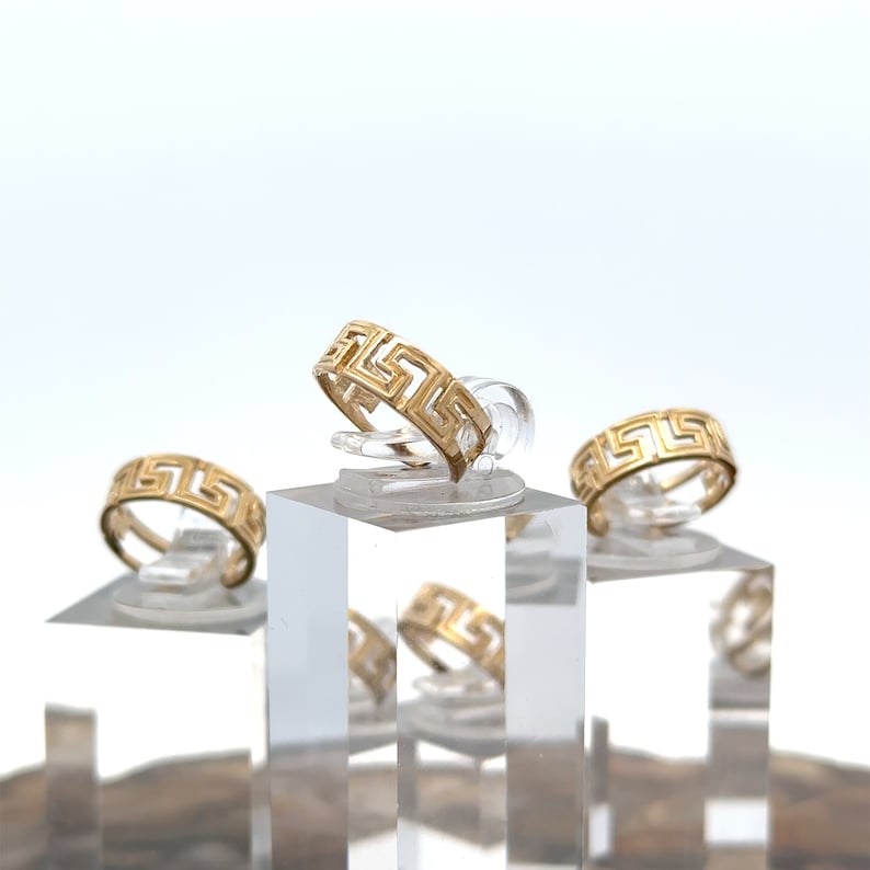 May include: Three gold rings with a Greek key design on a clear display stand. The rings are stacked on top of each other.