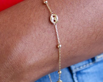May include: A delicate gold chain bracelet featuring small, evenly spaced round gold beads and two distinct, flat, circular gold charms with a central cutout design, creating a refined and minimalist look on the wrist.