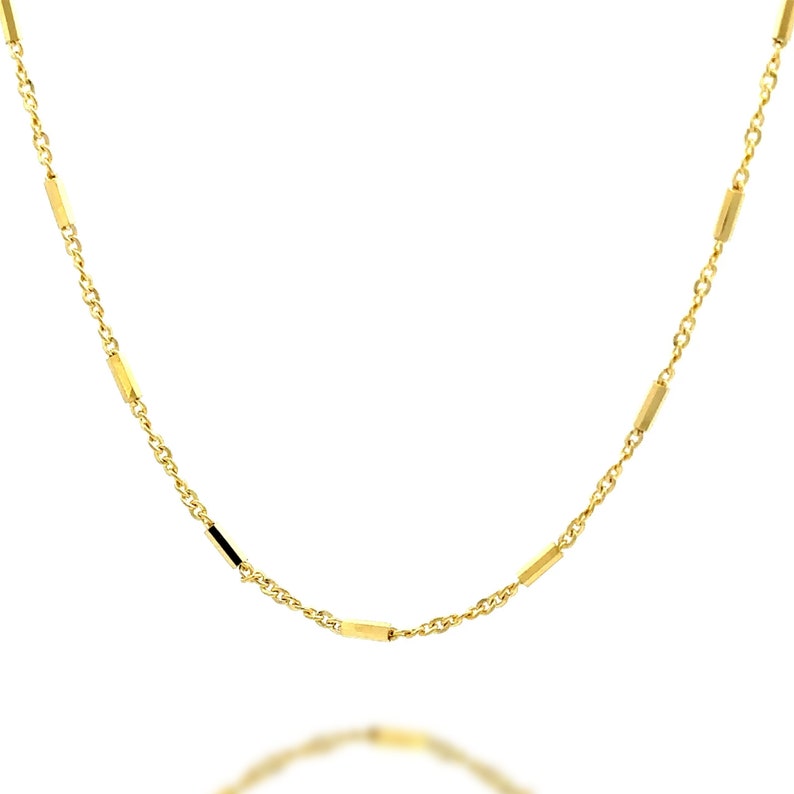 Puede incluir: Un collar de cadena dorada que presenta una serie de cuentas de barra doradas y pulidas, espaciadas uniformemente e integradas en el dise&ntilde;o de la cadena de eslabones finos. El collar muestra un acabado met&aacute;lico brillante y reflectante.