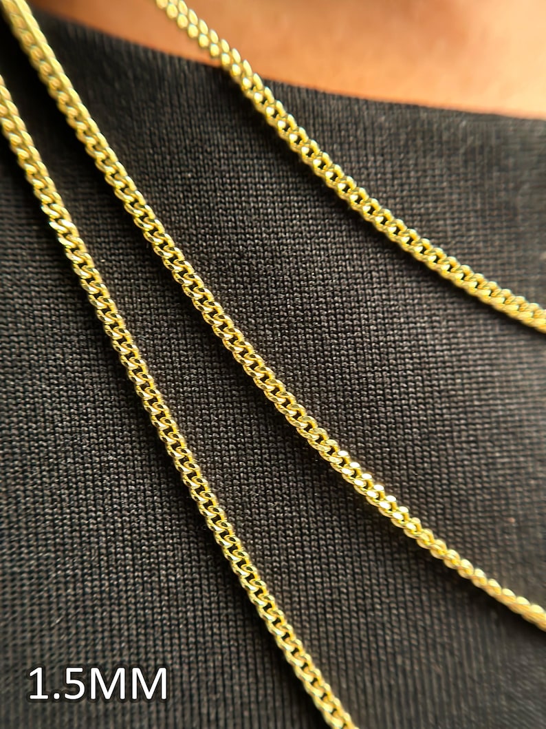 May include: Three gold-colored curb chains are displayed, each featuring a classic interlocking link design. The chains are arranged in parallel lines, and the text 1.5MM is clearly visible in the bottom left corner, indicating the width of the links.