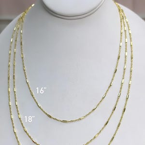 Puede incluir: Tres collares de cadena en tono dorado con peque&ntilde;os eslabones cil&iacute;ndricos espaciados uniformemente. Los collares se muestran en longitudes de 16, 18 y 20 pulgadas, con las medidas correspondientes impresas claramente junto a cada cadena.