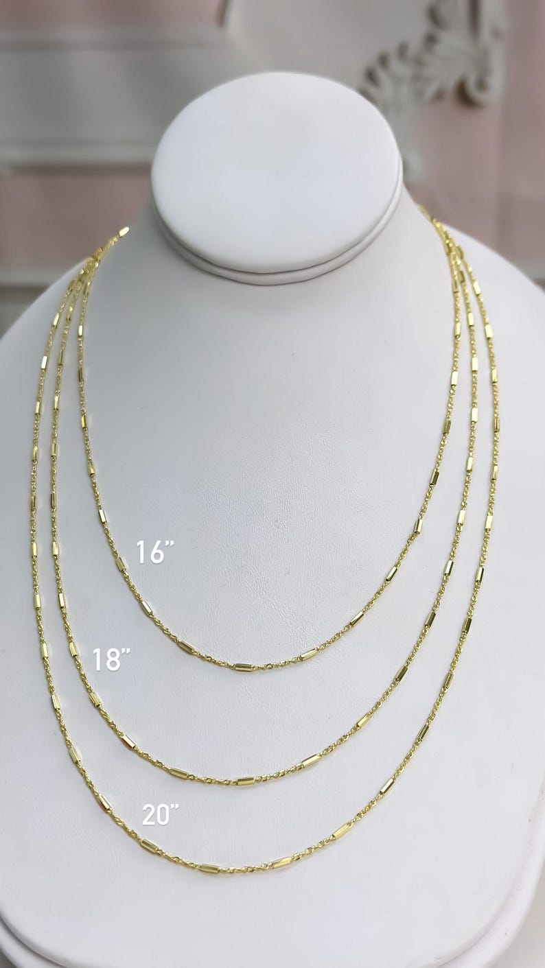 Puede incluir: Tres collares de cadena en tono dorado con peque&ntilde;os eslabones cil&iacute;ndricos espaciados uniformemente. Los collares se muestran en longitudes de 16, 18 y 20 pulgadas, con las medidas correspondientes impresas claramente junto a cada cadena.