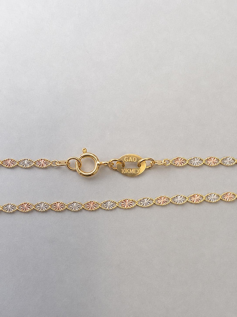 Puede incluir: Primer plano de un collar de oro con una cadena delicada. La cadena presenta un patr&oacute;n repetido de peque&ntilde;os eslabones ovalados en oro, oro rosa y plata. El cierre es visible y la etiqueta dice "GAO 10K MEX".