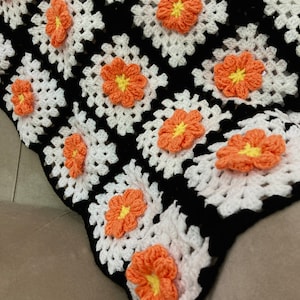 May include: A crocheted blanket with a black and white pattern and orange flowers.