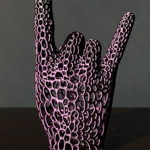 May include: A purple 3D printed hand sculpture in the shape of the rock and roll hand gesture. The sculpture is made of a lattice-like material.