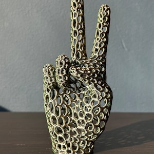 May include: A gold-colored metal sculpture of a hand making the peace sign. The hand is made of a latticework design.