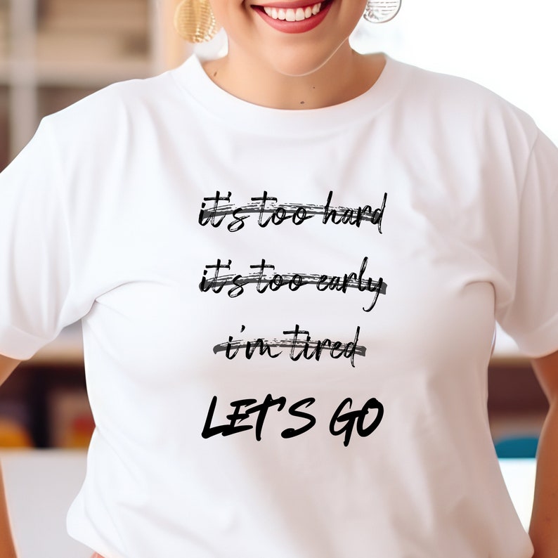 K&ouml;nnte beinhalten: Wei&szlig;es T-Shirt mit schwarzem Text: "It's too hard, It's too early, I'm tired, LET'S GO." Der Text ist handschriftlich. Das T-Shirt hat kurze &Auml;rmel.